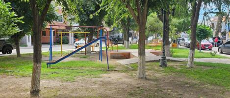 A park with playground equipment, trees, and a building in the background.