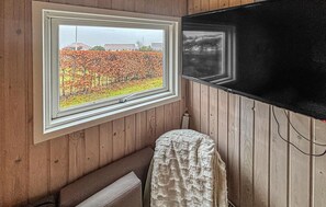 Een kamer met een raam dat uitkijkt op een tuin, houten wanden, een radiator en een zwarte tv die aan de muur is bevestigd.