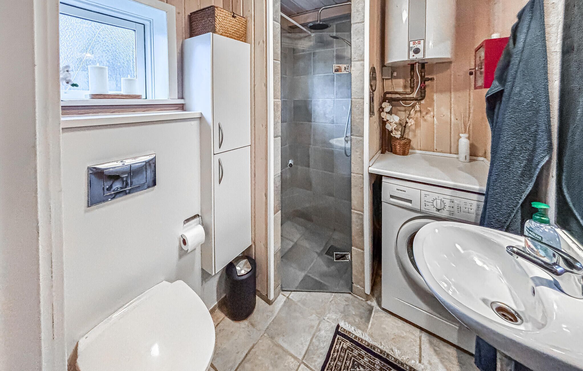 Un baño pequeño con inodoro, cabina de ducha, lavamanos y lavadora.