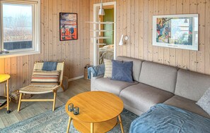 Una sala de estar acogedora con un sofá, un sillón de mimbre, una pequeña mesa de madera y una ventana con vistas al exterior.