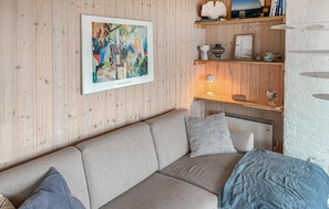Una sala de estar acogedora con una pared de madera, un cuadro abstracto enmarcado, un sofá con cojines estampados y una estantería con objetos decorativos.