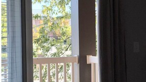 A view through a window with blinds, a white railing, and a dark curtain.