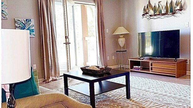A living room with a sofa, coffee table, lamp, TV, and artwork.