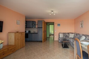 A living room with a sofa, a TV, a wooden cabinet, and a kitchen area with cabinets and a microwave. - Magda 2 Apt with Panoramic Sea View, Plomin, Croatia (Plomin)