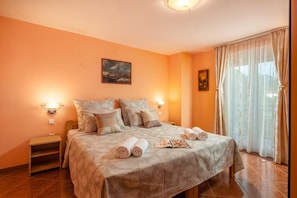 Habitación de hotel con una cama, dos mesitas de noche, un buró, un cuadro en la pared y una ventana con cortinas.
