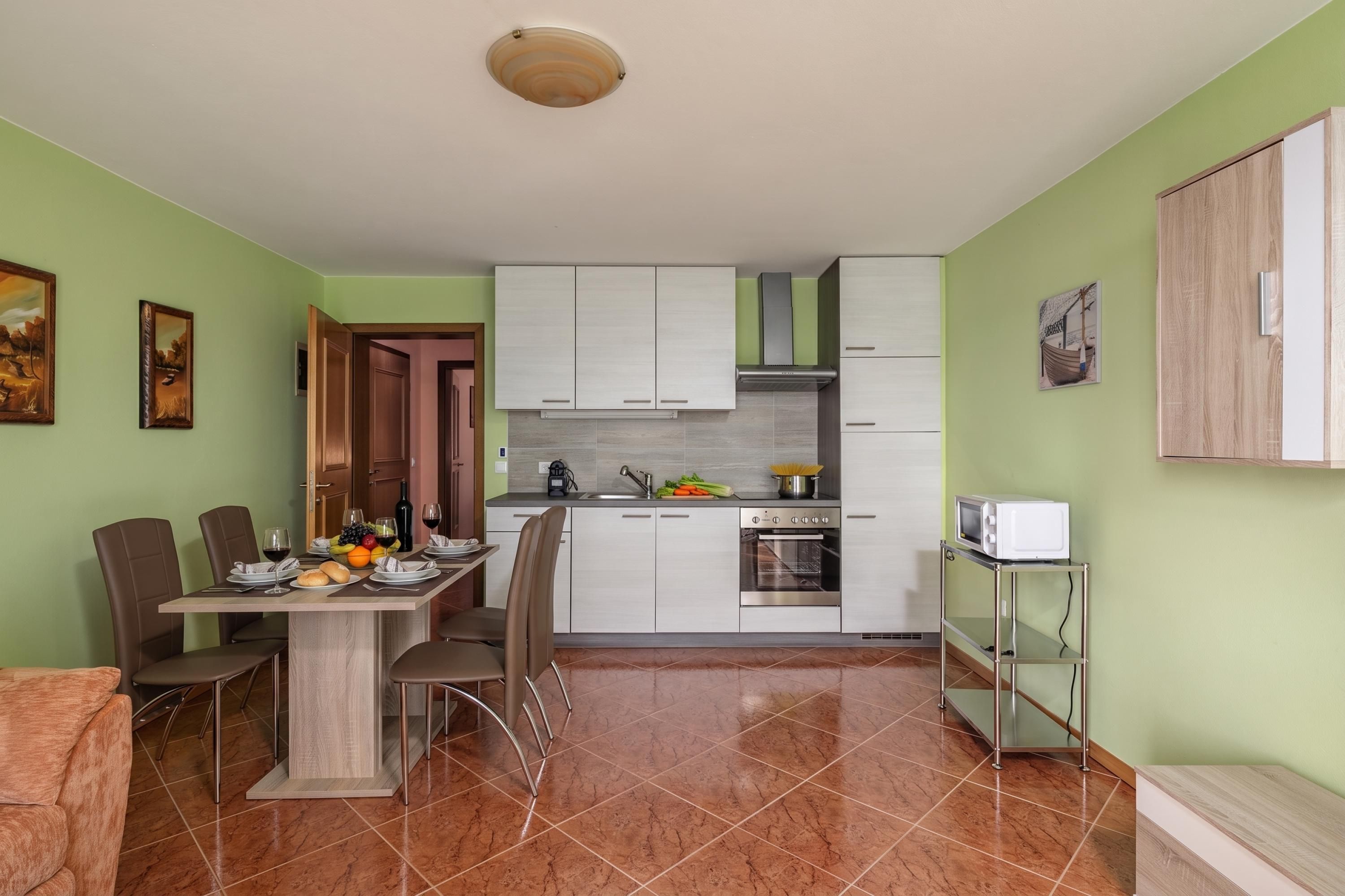 A compact kitchen with a dining area, featuring a stove, oven, and a microwave on a metal cart.
