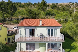 A two-story building with a red-tiled roof, a balcony with white railings, and a small window. - Magda 1 Apt with Panoramic Sea View, Plomin, Croatia (Plomin)