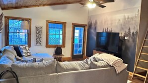 Una sala de estar acogedora con un sofá seccional, un televisor y un mural de un bosque en la pared.