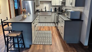 Una cocina moderna con una isla central, muebles de cocina blancos y un refrigerador de acero inoxidable.