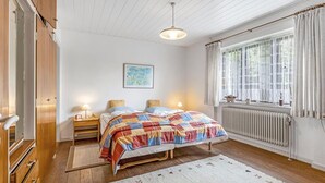 Ett sovrum med trägolv, en säng med ett färgglatt täcke, sänglampor, ett fönster med gardiner och ett element.