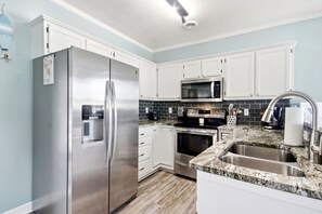 A modern kitchen with white cabinets, stainless steel appliances, a granite countertop, and a built-in oven. - Portobello II 1316 - 2nd Row Community in Garden City Beach (Garden City Beach)