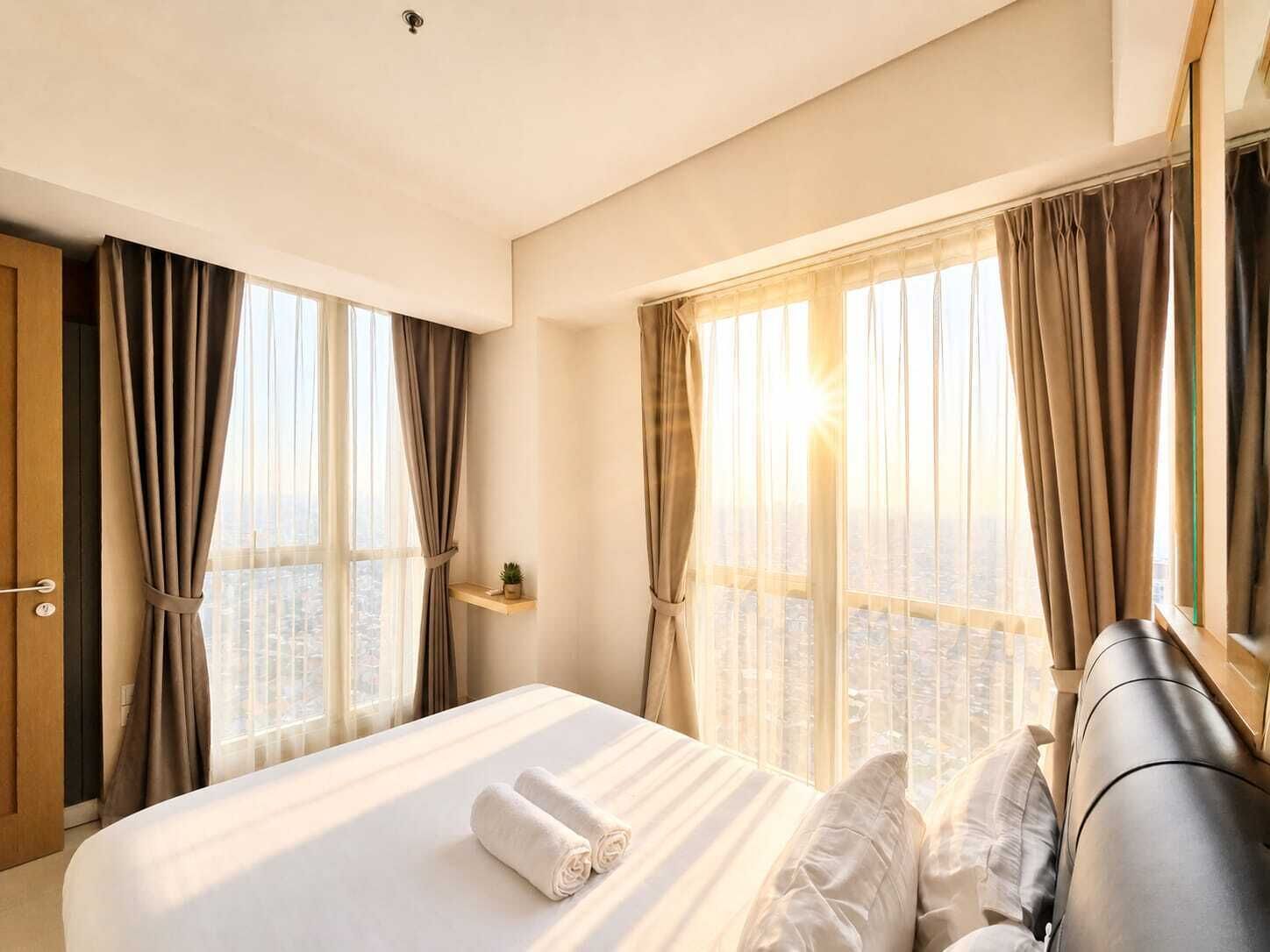 Habitación de hotel con cama, cortinas, vistas a la ciudad y un pequeño estante con una planta.