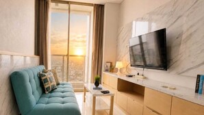 A modern living room with a sofa, a coffee table, a TV, and a city view. - Artisan By SanLiving - 2BR - Direct Mall (Jakarta)