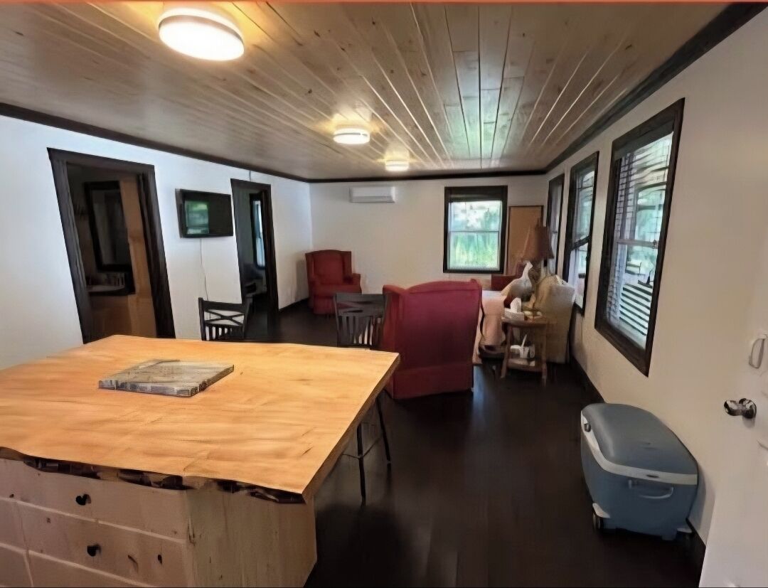 Une pièce avec un plafond en bois, une table à manger, une chaise rouge, une petite table sur laquelle se trouve une statue, et une valise bleue.