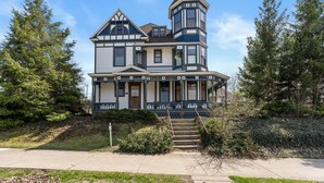Una casa de estilo victoriano con una torre destacada, un porche delantero y una escalera que conduce a la entrada.
