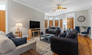 Ein Wohnzimmer mit Fernseher, Sofas, einem Couchtisch und einem Deckenventilator.