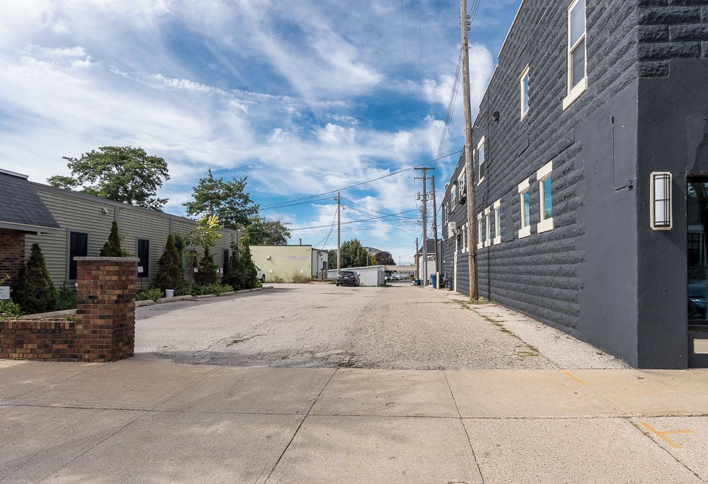 A residential street with houses, a gravel driveway, and utility poles.