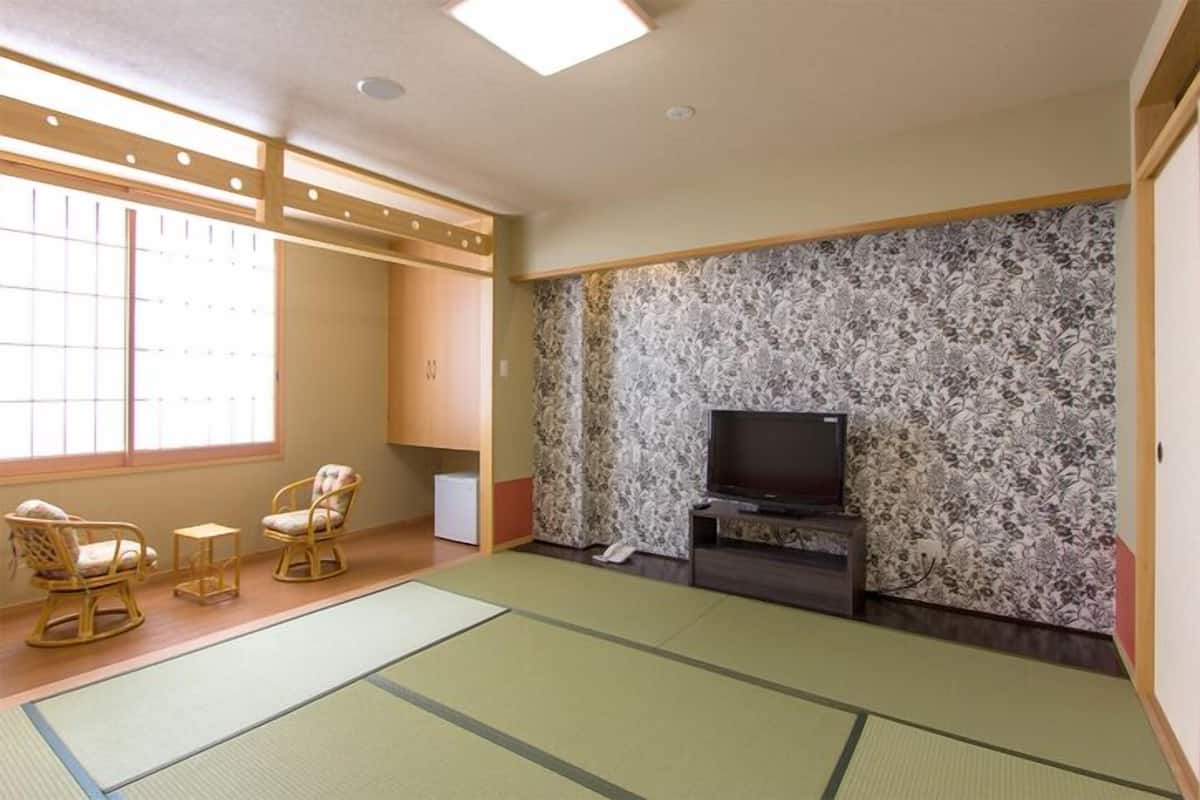 Una habitación japonesa tradicional con suelo de tatami, televisor y futón.