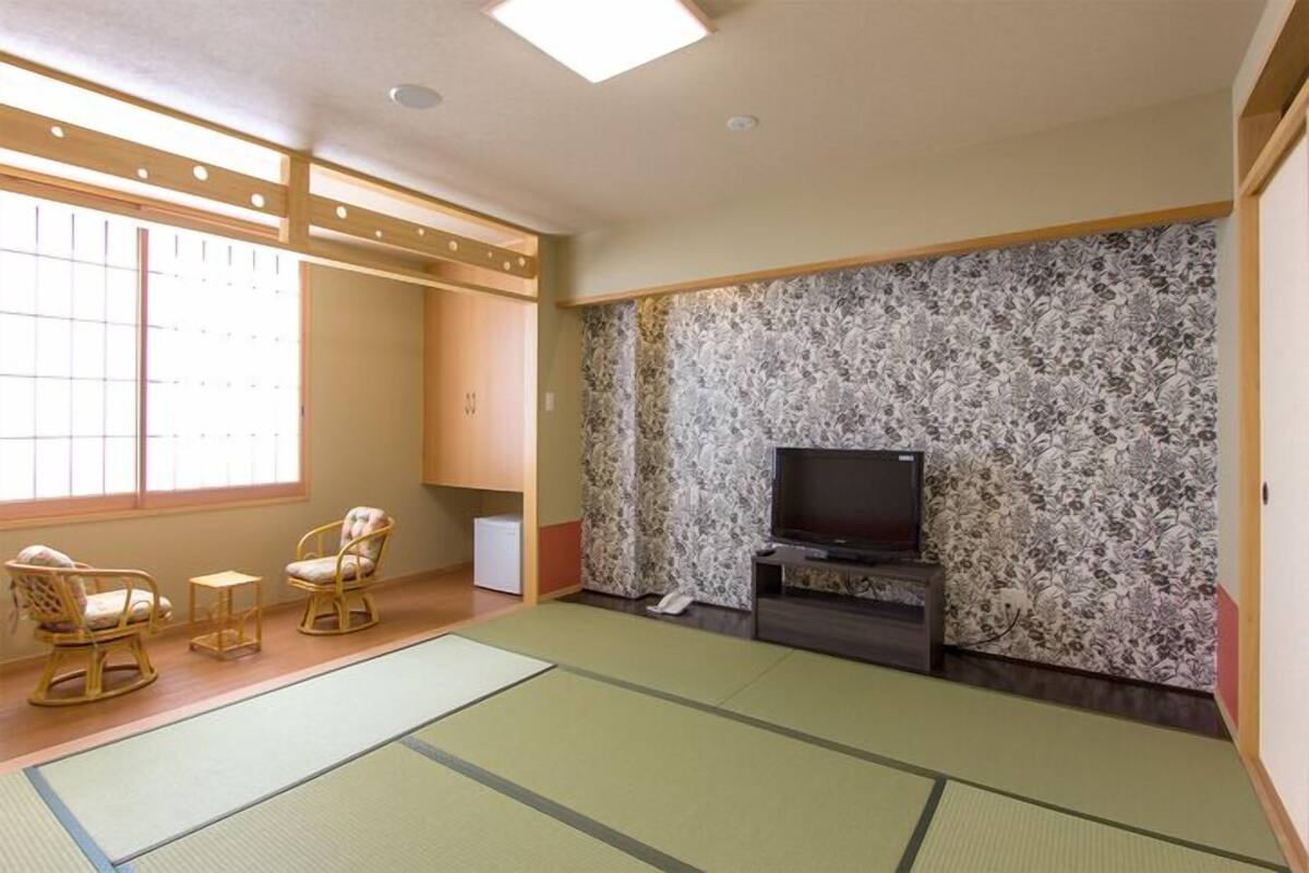 Una habitación japonesa tradicional con suelo de tatami, televisor y futón.