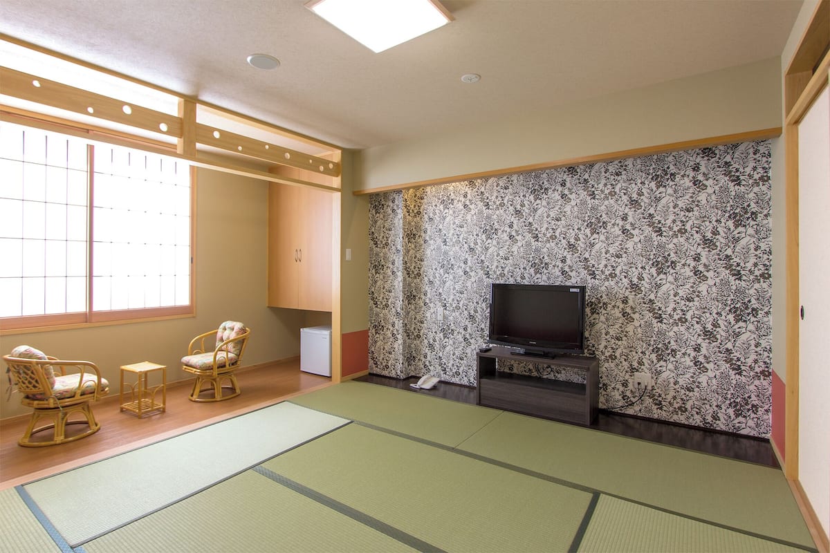 Una habitación con esteras de tatami, un televisor, dos sillas y una mesita.