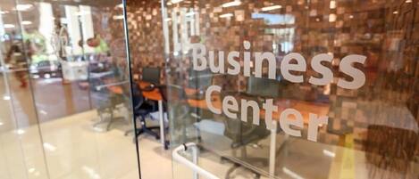 Un mur de verre sur lequel on peut lire « Centre d’affaires », et qui reflète l’intérieur, notamment des chaises et des bureaux.