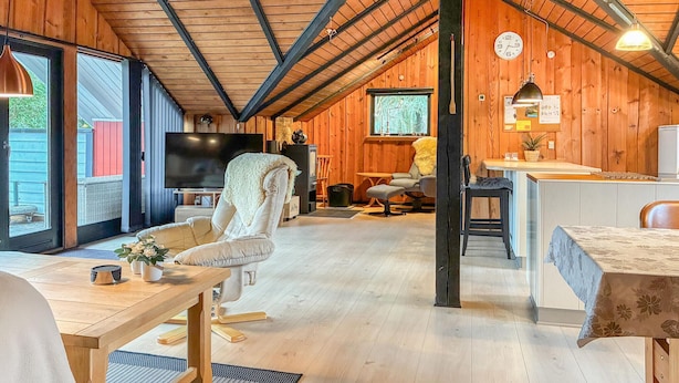 Interior acolhedor de uma cabana com teto de madeira, televisão, área de jantar e cozinha.