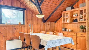 Uma sala de jantar de madeira com uma mesa, cadeiras, uma janela com vista e um armário com portas de vidro.