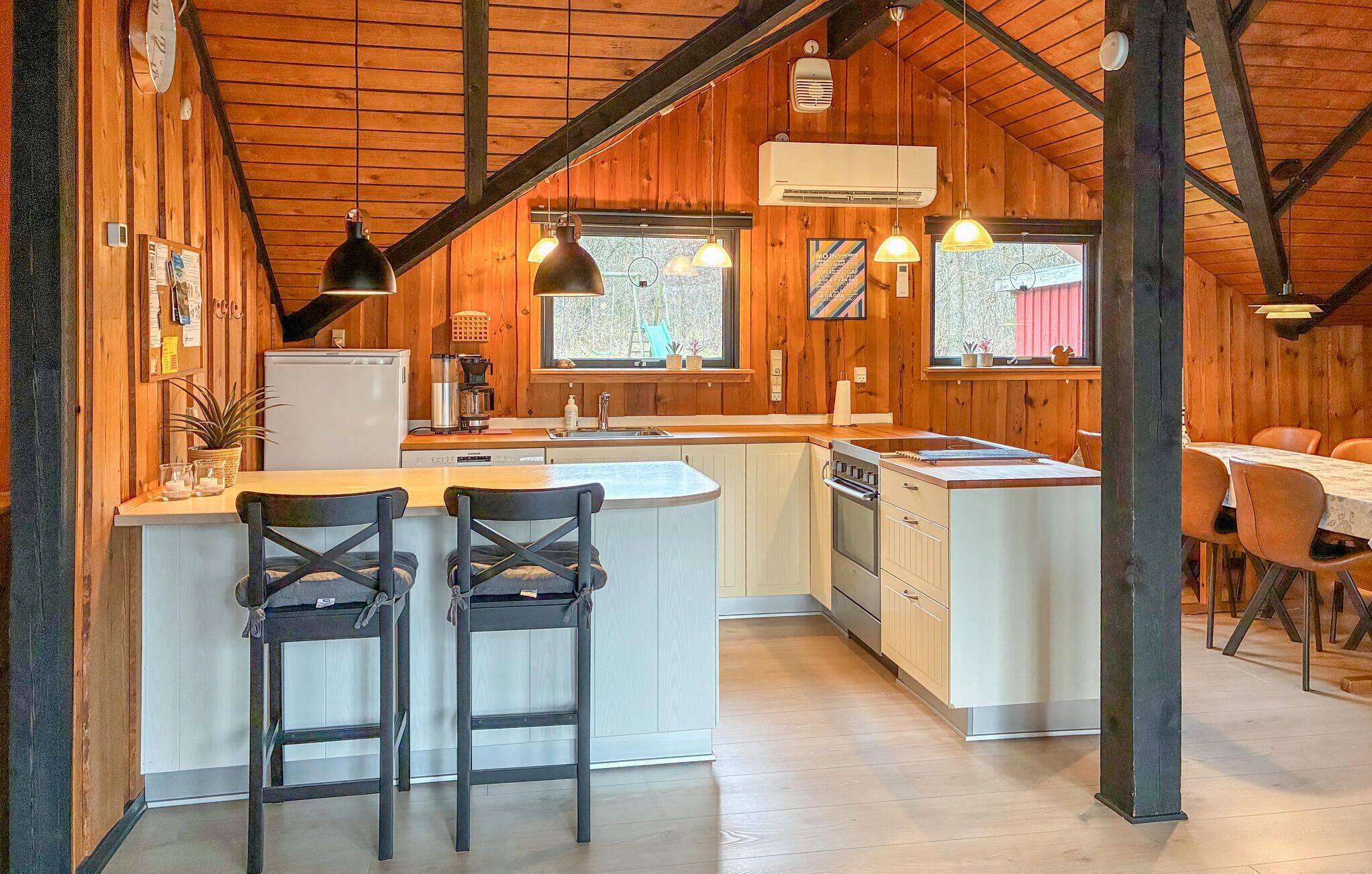 A cozy kitchen with wooden walls, a central island with bar stools, and pendant lighting.