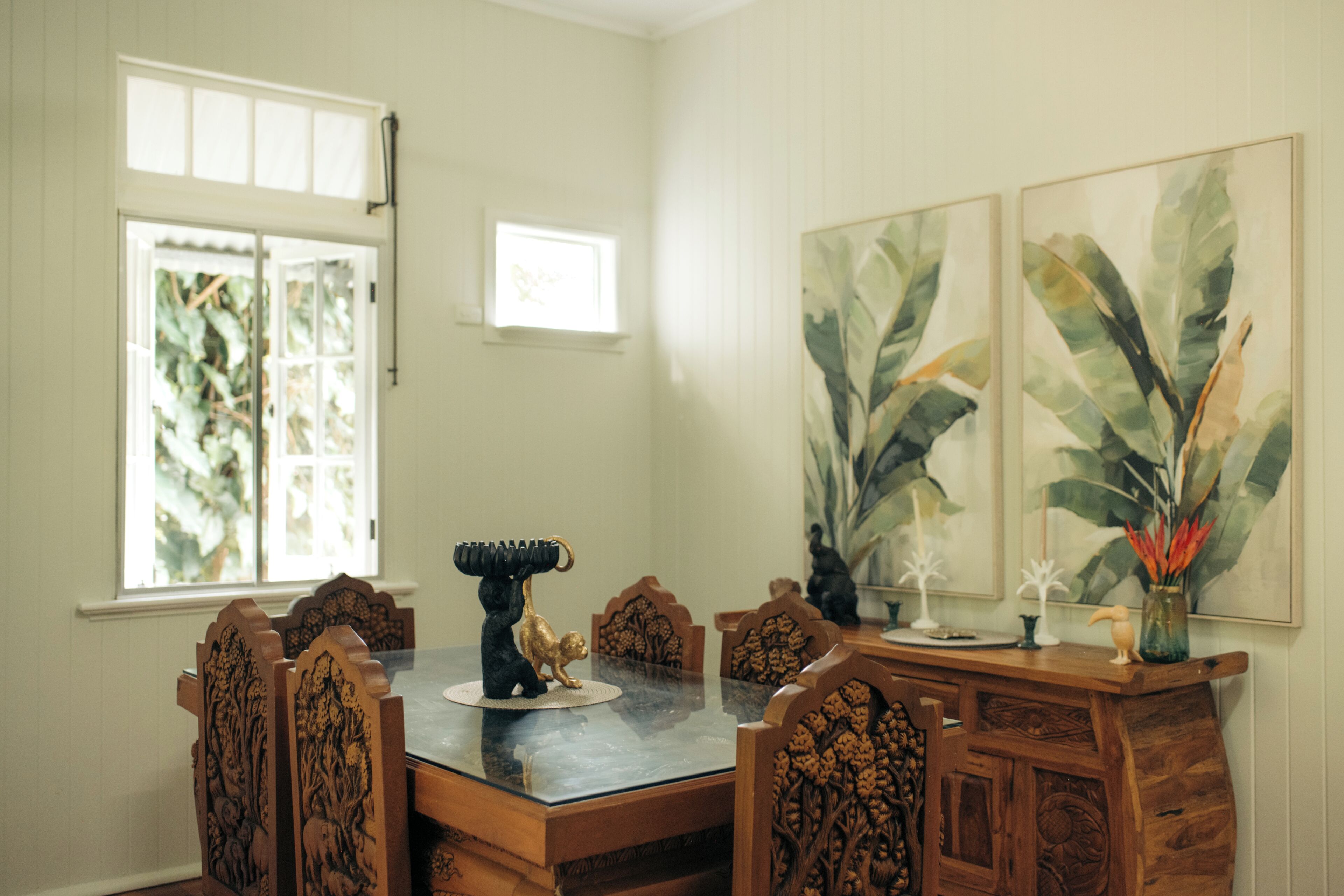 A dining area with a wooden table and chairs, a decorative centerpiece, and large botanical paintings on the wall.