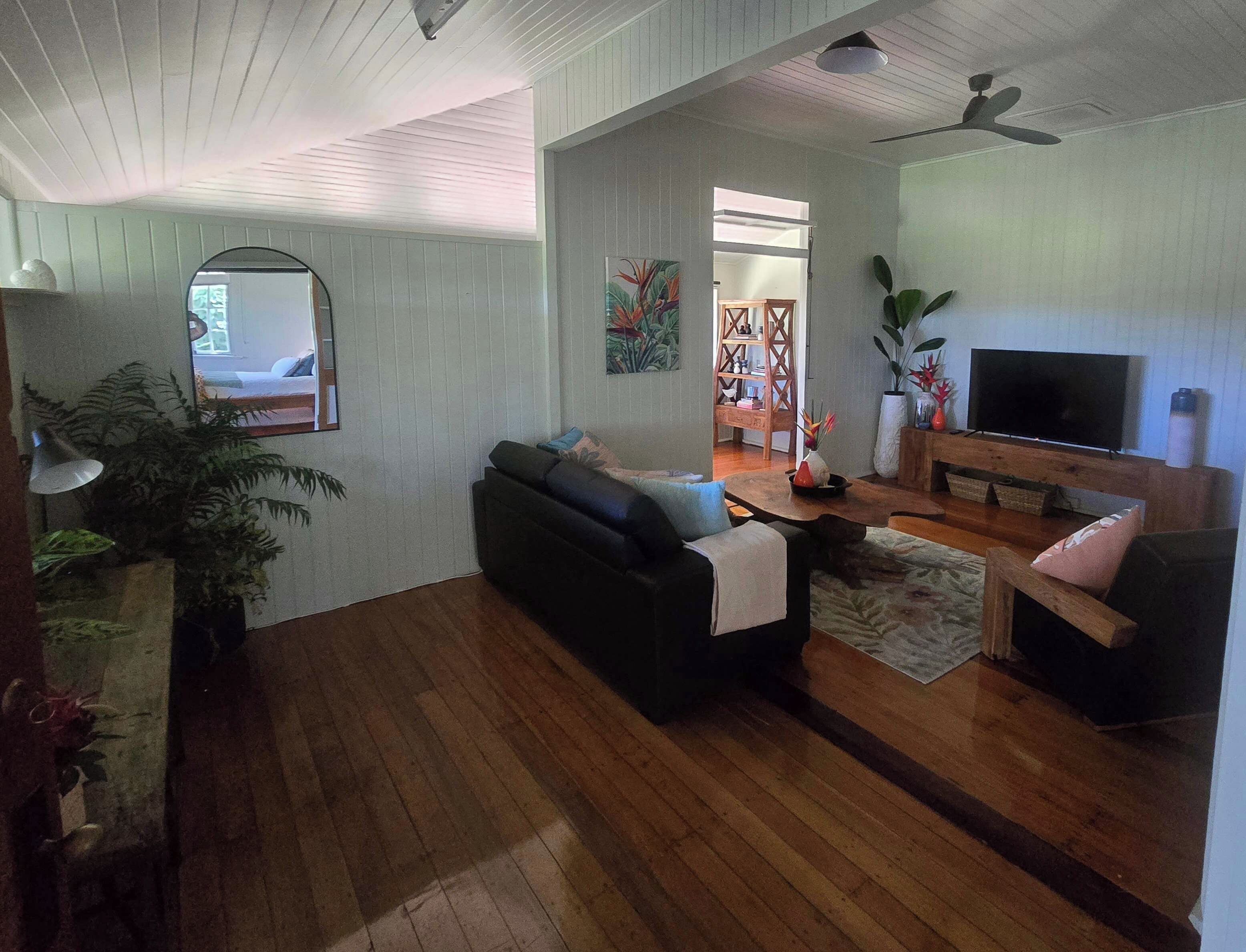 A living room with a black sofa, a wooden coffee table, a television, and a ceiling fan.