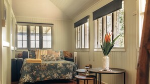 A room with a bed, a round table, and a window with a plant.