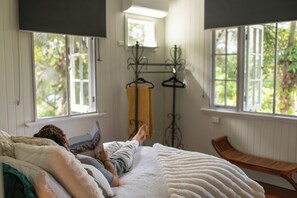 Une chambre à coucher avec un lit, une fenêtre, un banc en bois et un portant métallique avec des vêtements.