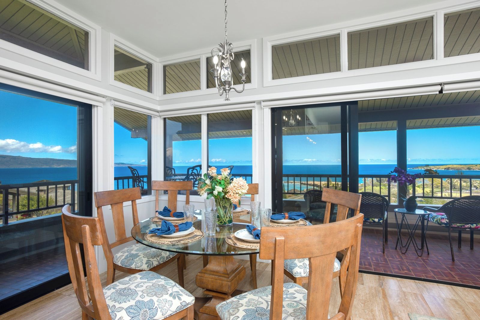 A dining area with a glass table, wooden chairs, and a view of the ocean.