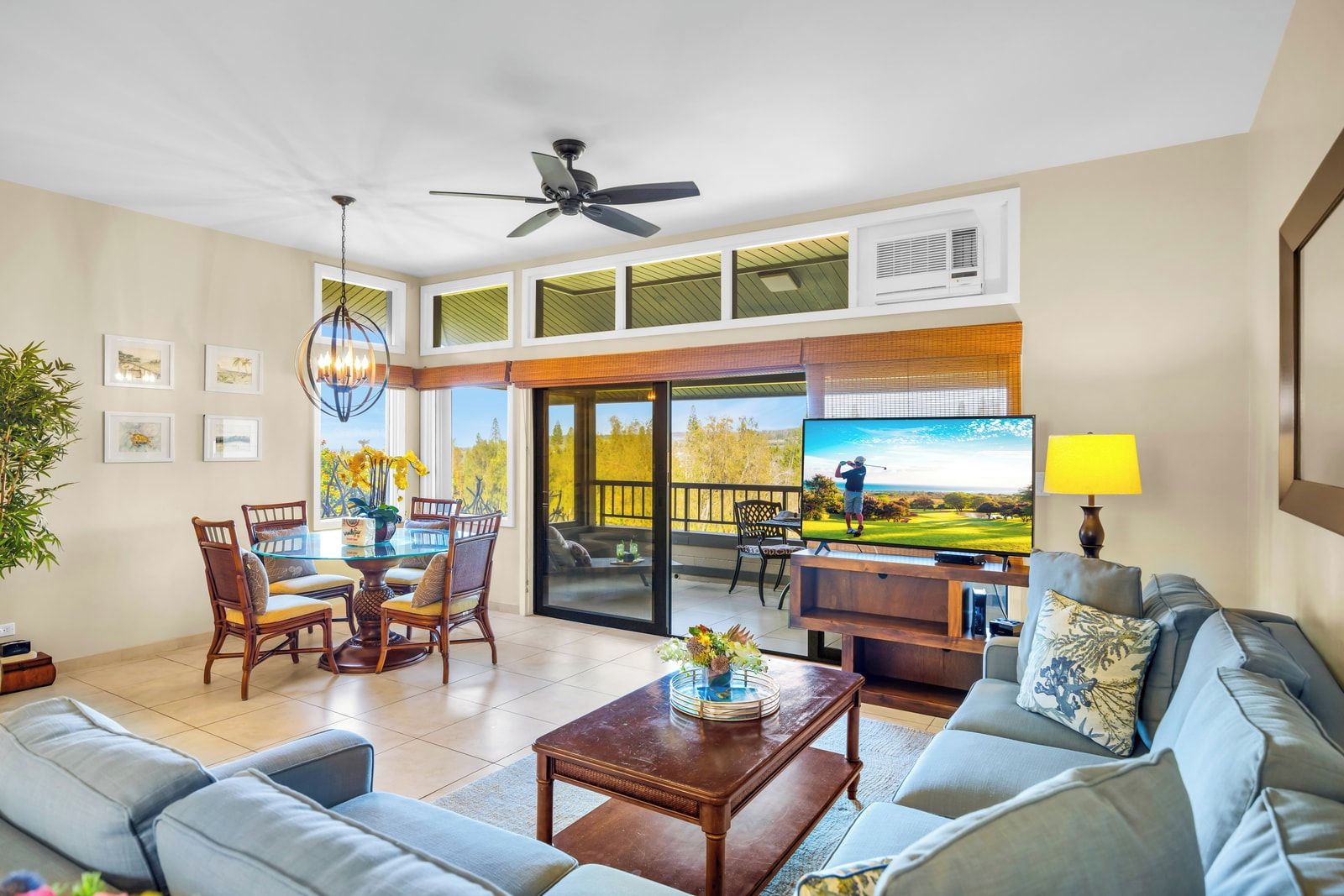 A spacious living room with a television, comfortable seating, a dining area, and a balcony with a view.