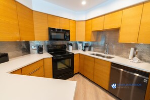 A modern kitchen with wooden cabinets, a stainless steel dishwasher, and a black microwave. - Blueberry Hill Condo - Free Parking, Pool and Hot Tub (Whistler)