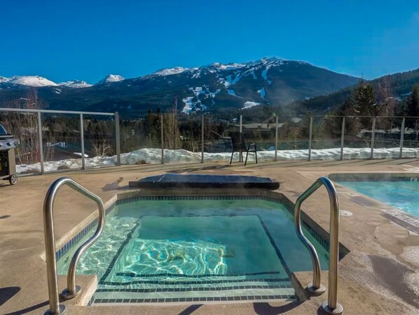 A pool with clear water, metal railings, and a mountain view in the background. - Blueberry Hill Condo - Free Parking, Pool and Hot Tub (Whistler)