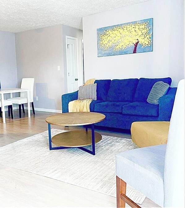 Un salon avec un canapé bleu, une table basse ronde et un fauteuil blanc.