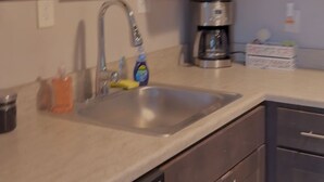 Una cocina con alacenas oscuras, un lavamanos de acero inoxidable, una cafetera y un lavavajillas.
