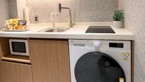Una cocina compacta con armarios de madera, microondas integrado, lavavajillas y un lavatorio.