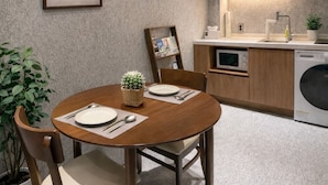 Cocina compacta con armarios de madera, un microondas y una lavadora. En primer plano, una mesa de comedor con sillas y un cactus como centro de mesa.