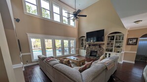 A spacious living room with a large sectional sofa, a fireplace, and a TV mounted above it. - Stunning 4-Bedroom Retreat with Resort-Style Backyard in
 charming Evans. (Evans)