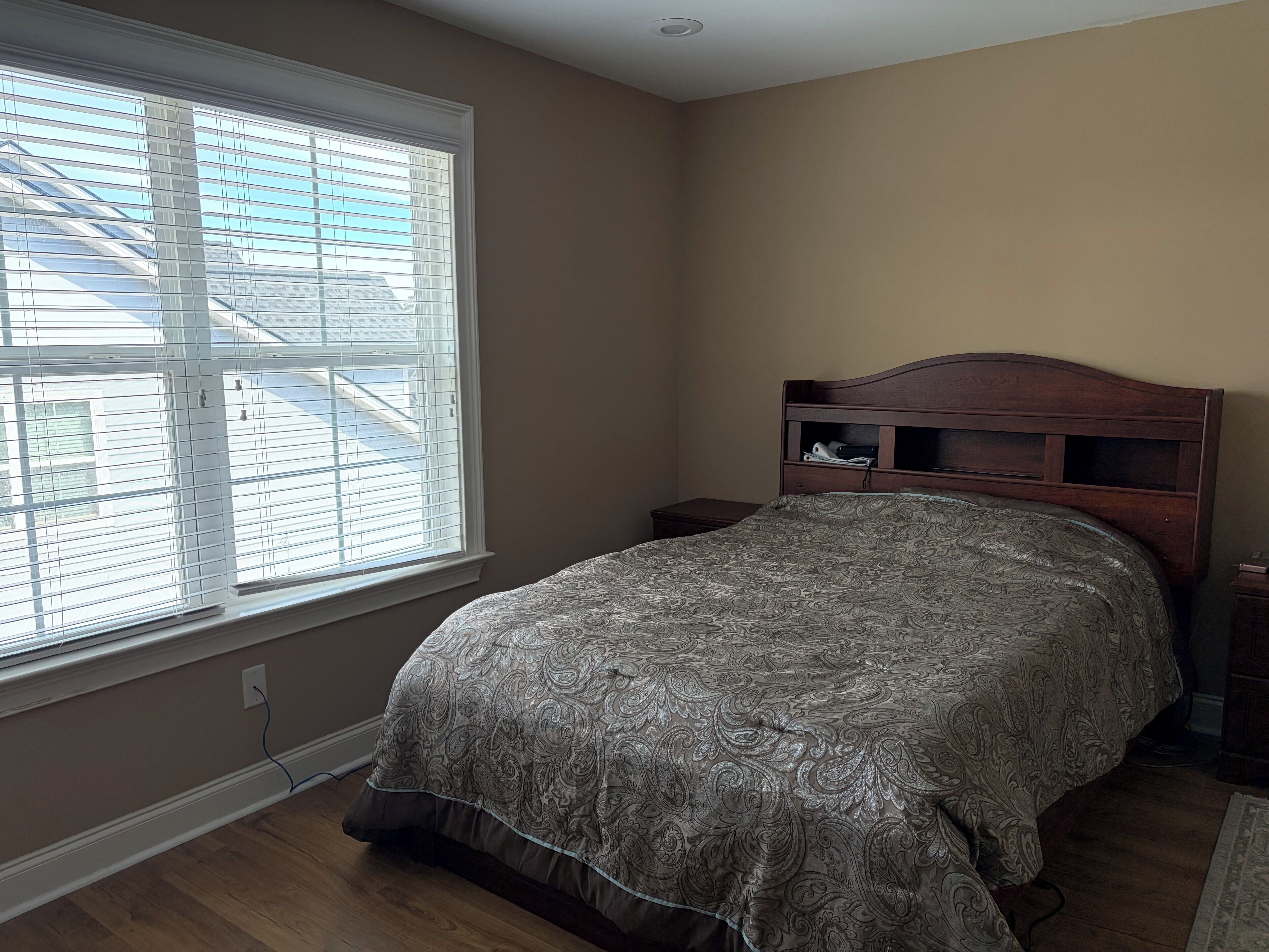 Une chambre avec une grande fenêtre, une tête de lit en bois et une couvre-lit à motifs.