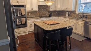 A kitchen with white cabinets, a granite countertop, a central island with bar stools, a refrigerator, and a window with blinds. - Stunning 4-Bedroom Retreat with Resort-Style Backyard in
 charming Evans. (Evans)