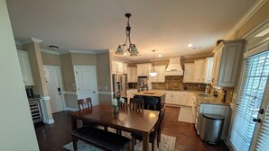 A spacious kitchen with white cabinets, a central island, and a dining area with a bench. - Stunning 4-Bedroom Retreat with Resort-Style Backyard in
 charming Evans. (Evans)