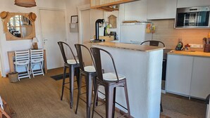 A compact kitchen with a central island, bar stools, a hanging light fixture, and wooden cabinets. - Beautiful 2-room apartment with Wi-Fi and mooring – View over the canals of Port Grimaud (PORT GRIMAUD)