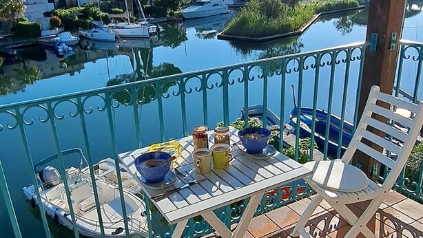 A balcony with a table and chairs, overlooking a marina with boats and greenery. - Beautiful 2-room apartment with Wi-Fi and mooring – View over the canals of Port Grimaud (PORT GRIMAUD)