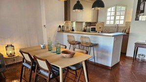 Un comedor con mesa y sillas de madera, una cocina al fondo y una ventana con vistas.