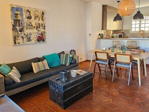 Ein gemütliches Wohnzimmer mit einer Couch, einem Esstisch mit Stühlen und einer Küchenzeile mit Pendelleuchte.