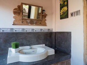A bathroom with a white sink, a small potted plant, a wooden mirror, and a wall-mounted light switch. - Villa Rumah Manis (Gili Trawangan)