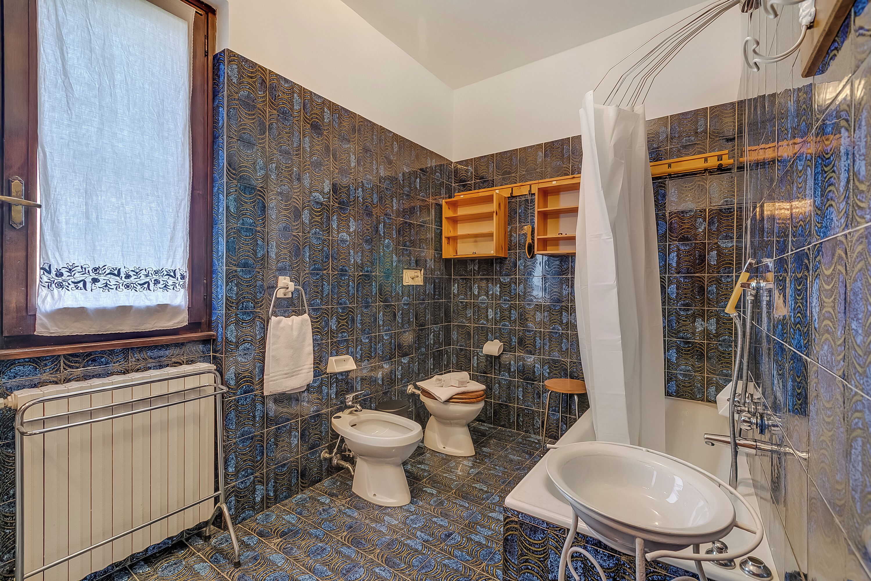 A bathroom with a radiator, two toilets, a bathtub, and a shower curtain.